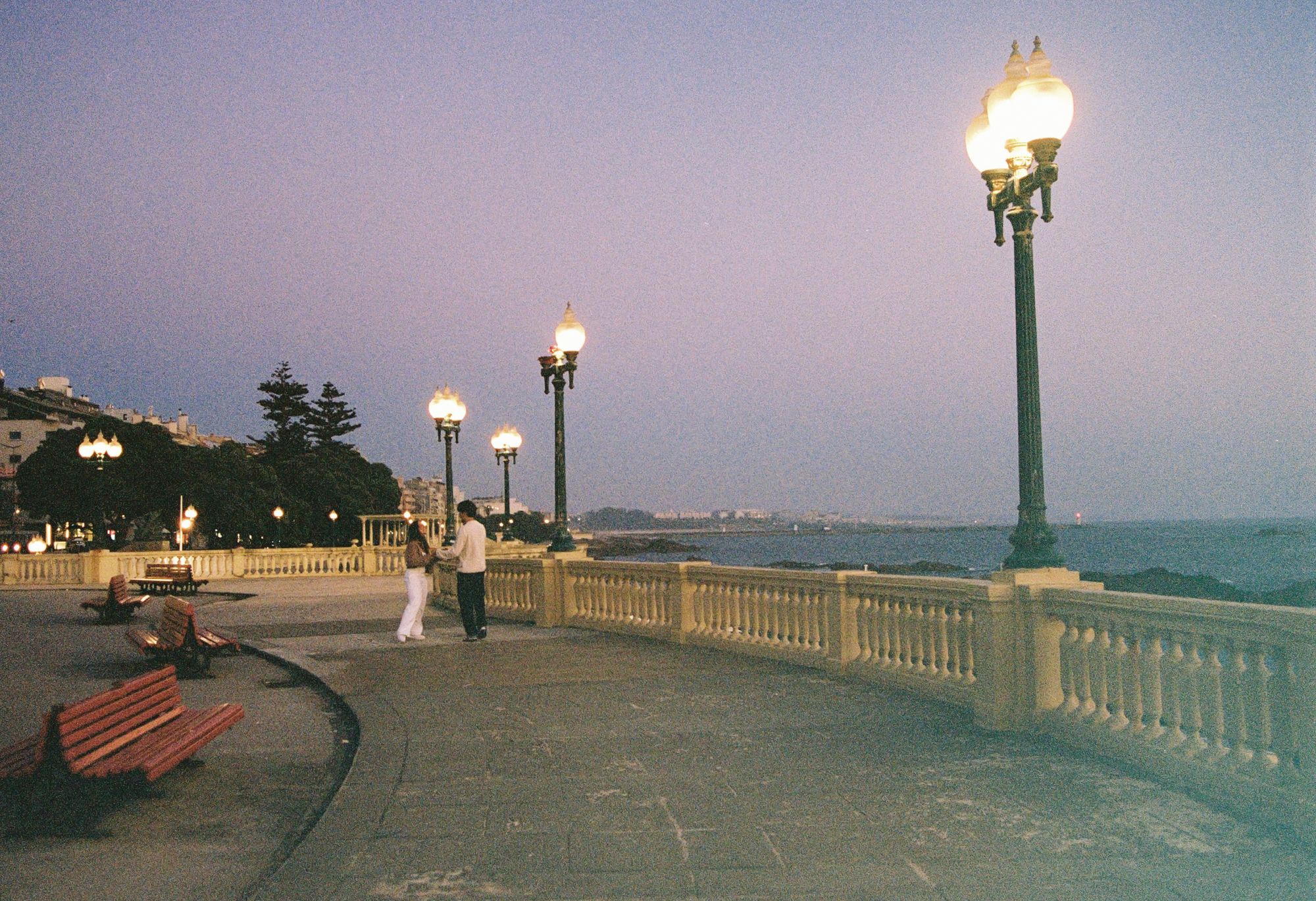 Casal a conversar numa avenida junto ao mar ao entardecer, fotografia analógica